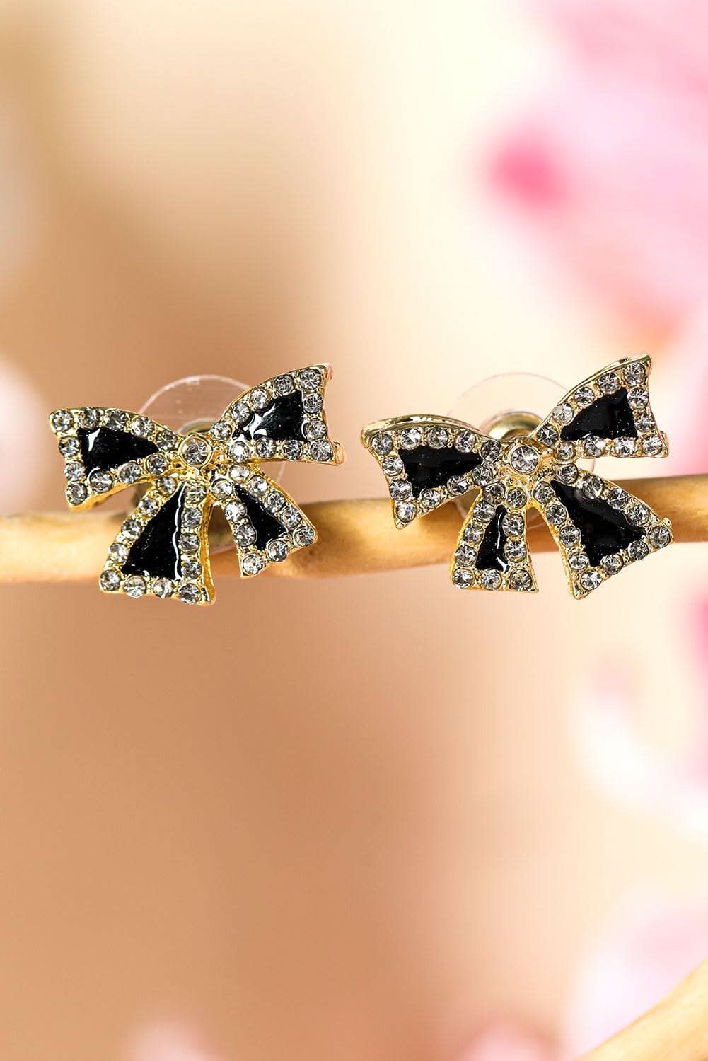 Black rhinestone bow knot stud earrings with gold accents on a soft pink background