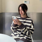 Woman wearing black and white striped loose cotton pullover sweatshirt using smartphone