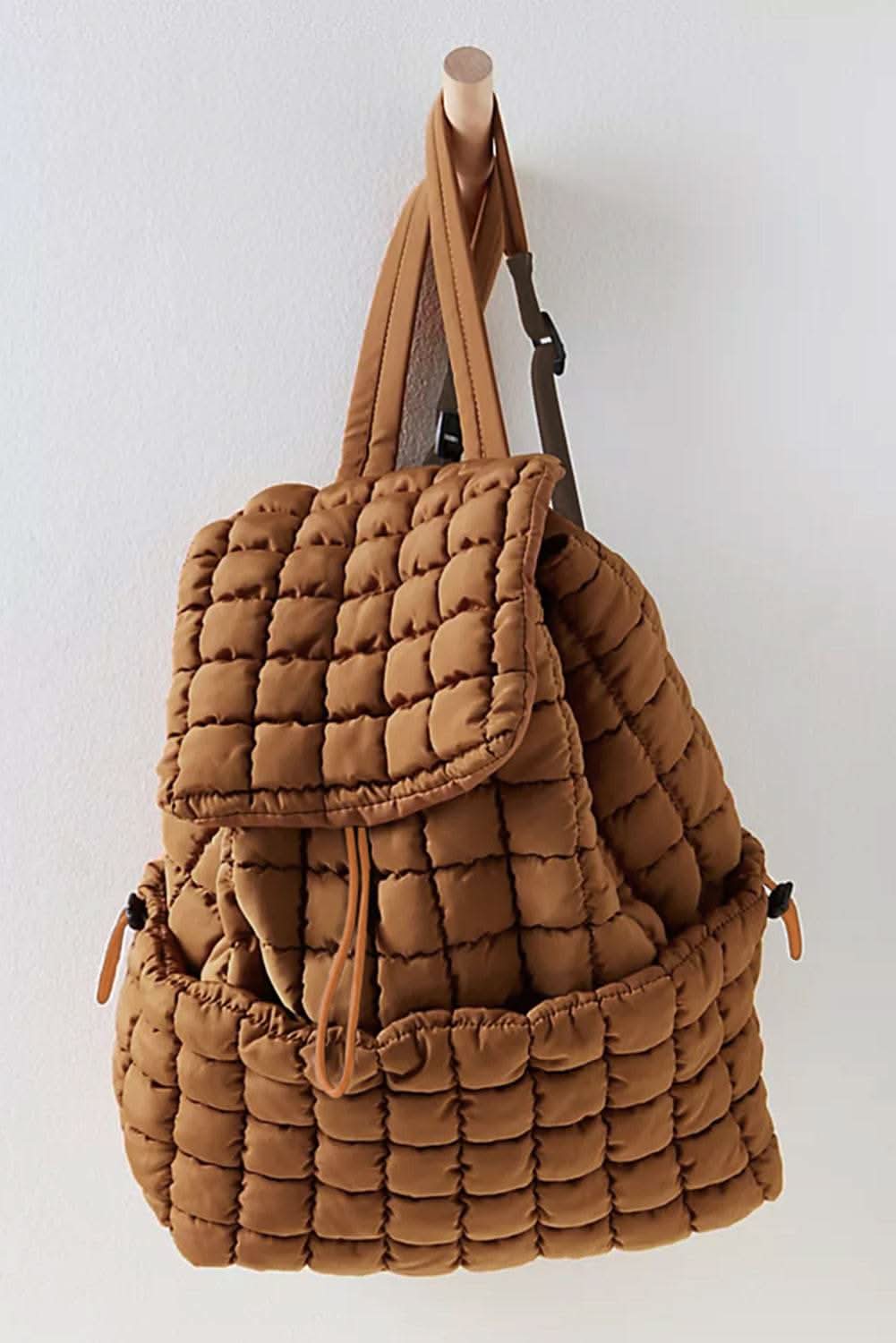 Coffee solid flapped quilted puffer backpack hanging on wooden hook on white wall
