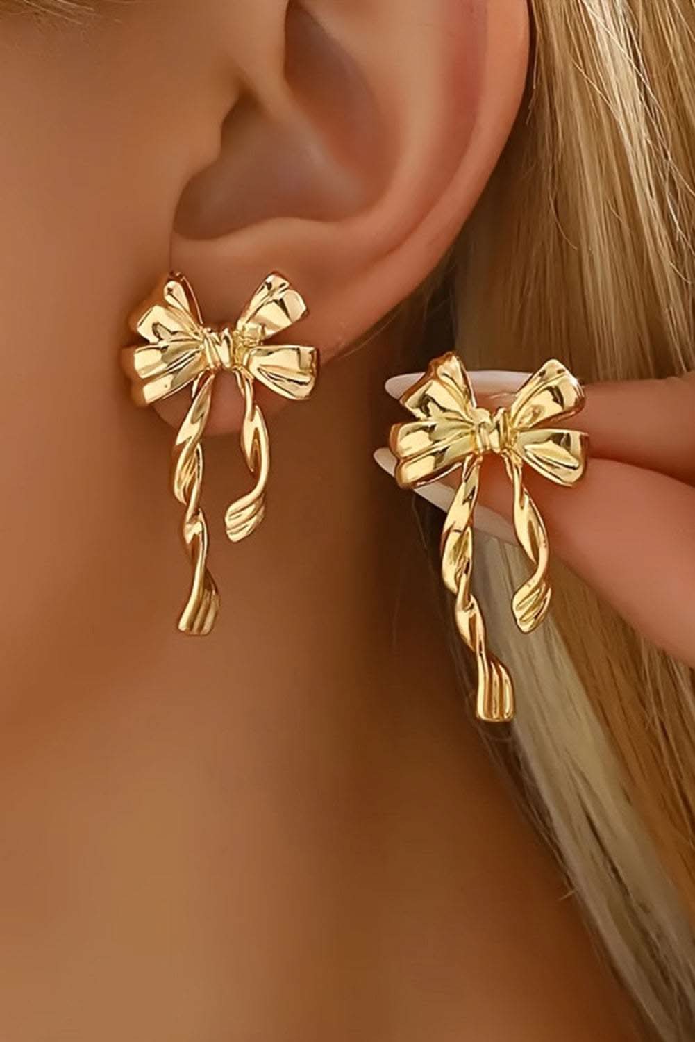 Gold bow knot plated alloy stud earrings worn on ear with feminine elegant design
