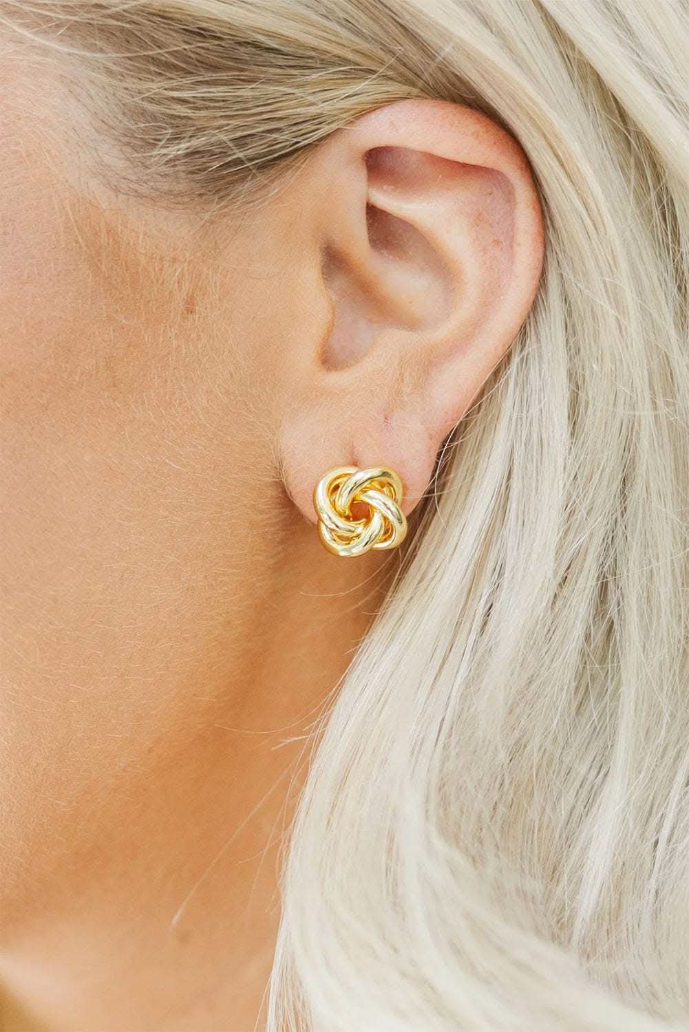 Close-up of gold minimalism knotted plated stud earrings on ear