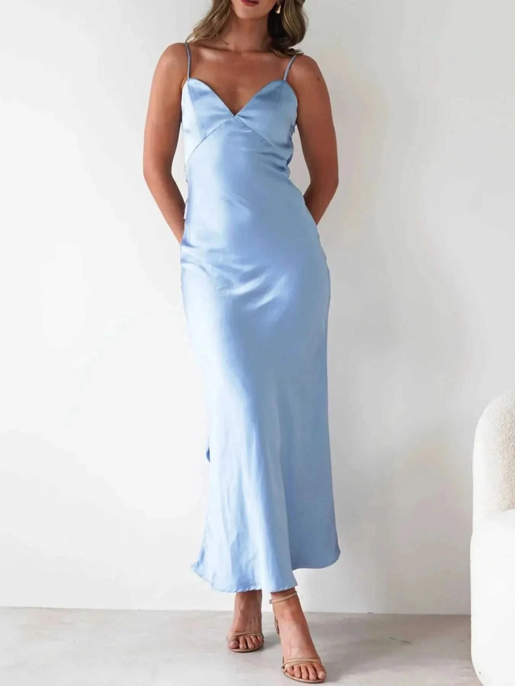 Woman wearing light blue satin backless cami dress with thin straps and midi length