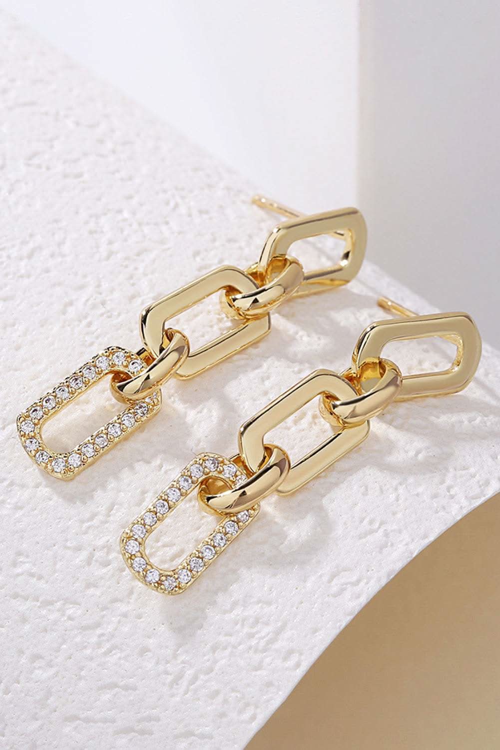 Gold chain link rhinestone decor plate stud earrings on white textured surface