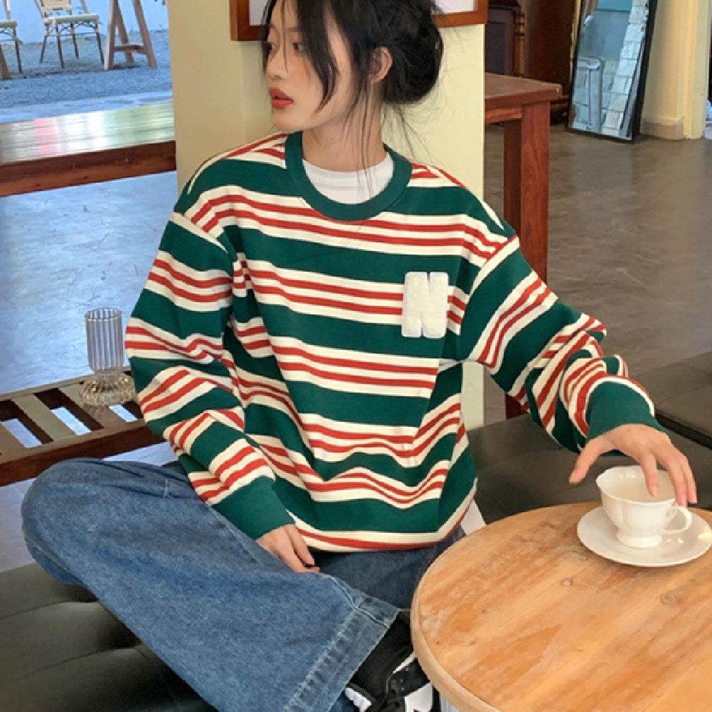 Woman wearing retro alphabet embroidered striped sweater sitting at table with a cup