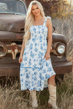 Woman wearing sky blue floral print sleeveless long dress with shirred bodice and knot shoulder straps outdoors