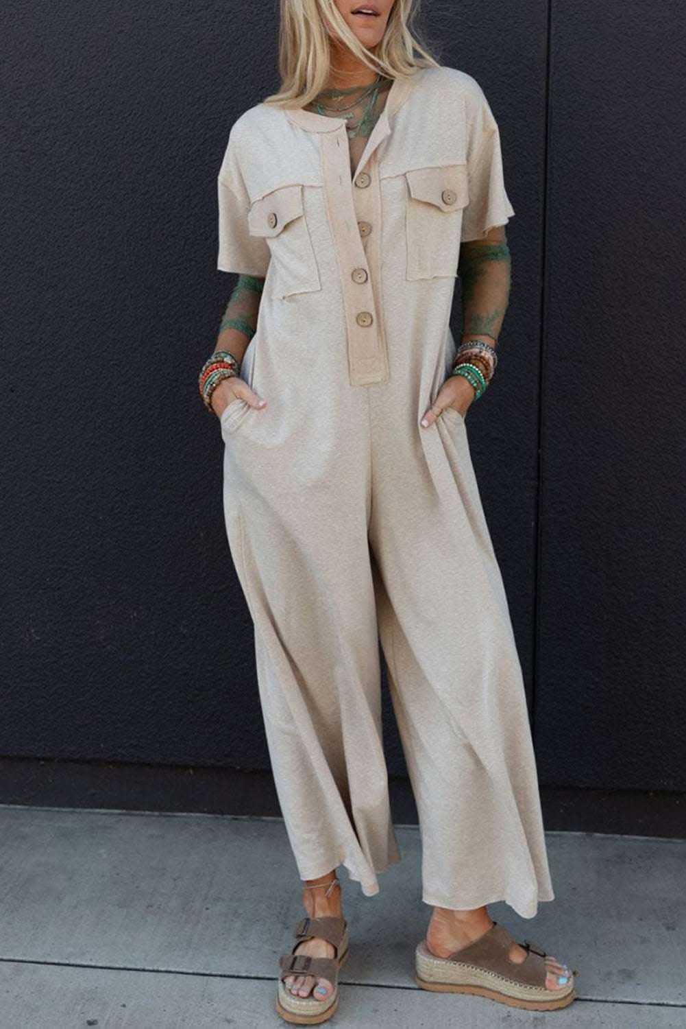 Beige jumpsuit with half placket, chest pockets, short sleeves, and wide leg design for casual wear.