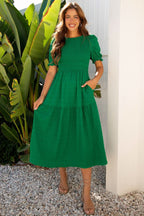 Woman wearing a dark green solid textured smocked puff short sleeve high waist long dress standing outdoors with greenery background