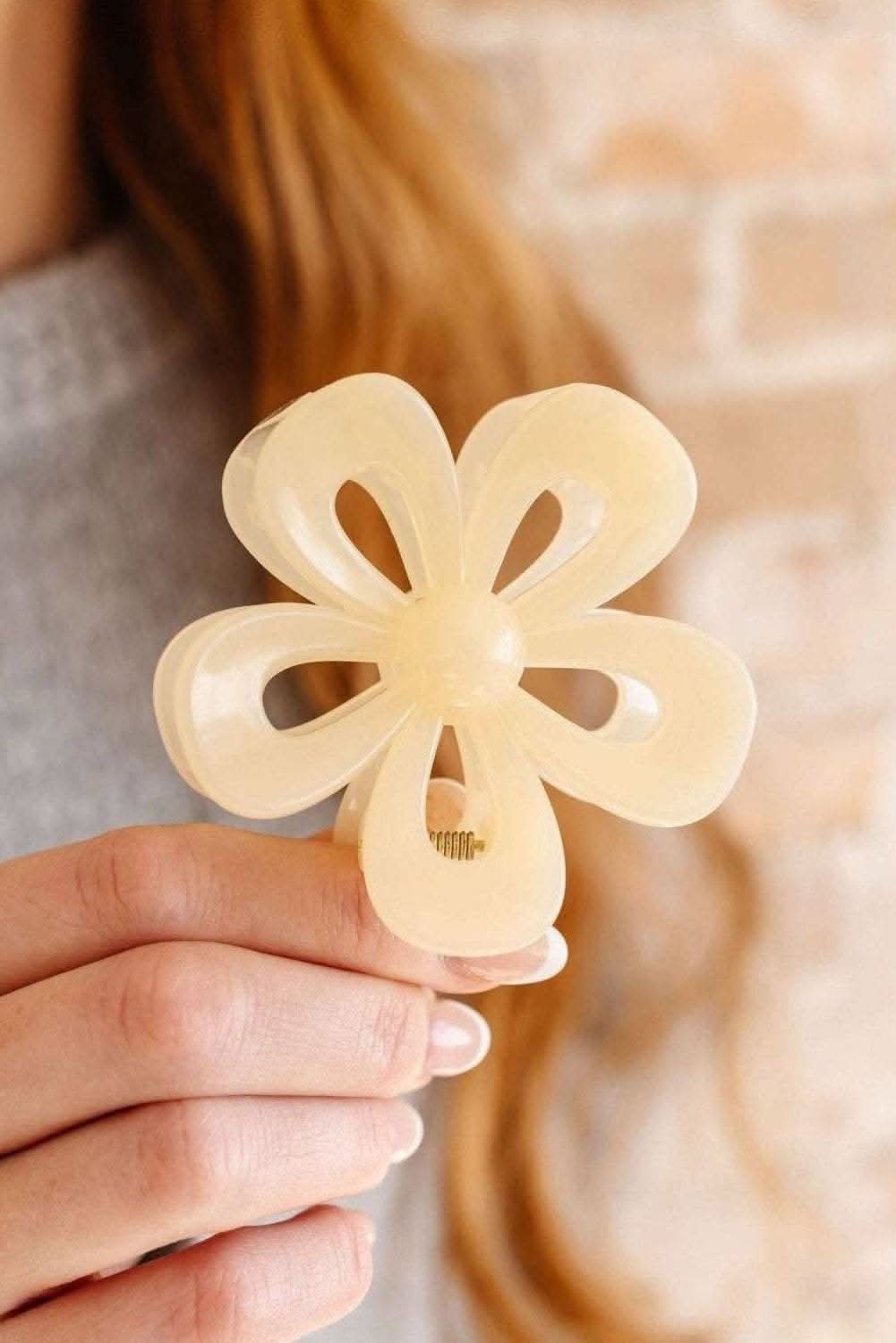 Cream-colored flower shape resin hair clip held by hand