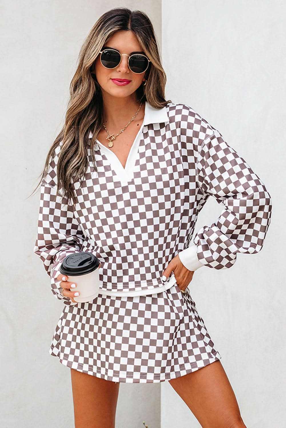 Woman wearing khaki checkered print polo collar cropped long sleeve top and drawstring mini skirt set holding coffee cup