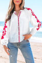 White floral embroidered puff long sleeve casual shirt with red floral details on sleeves and front trim, paired with blue jeans at the beach.