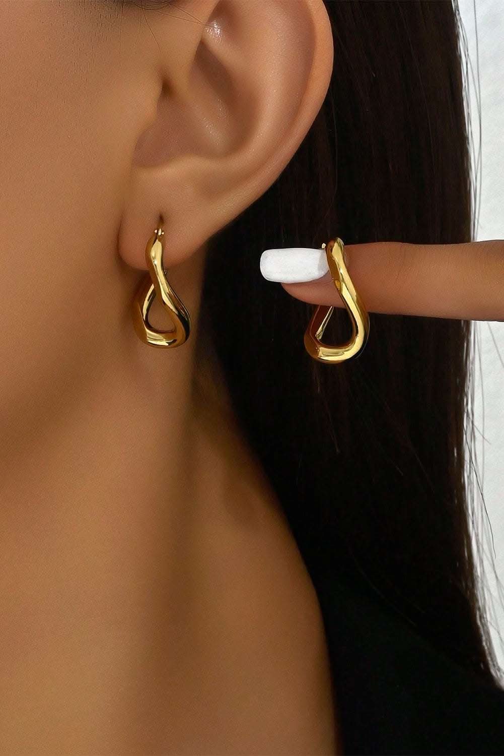 Gold plated 3D spiral twisted hoop earrings worn on ear with glossy finish
